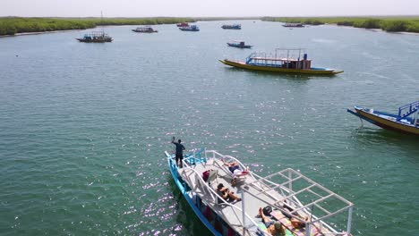 Antenne-über-Einem-Hölzernen-Touristenboot,-Das-Einen-Kleinen-Hafen-Verlässt-Und-Den-Gambie-Fluss-In-Der-Nähe-Von-Banjul-Gambia-Hinaufführt-1