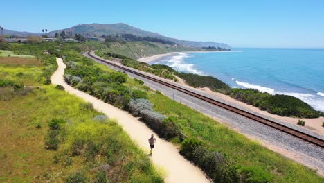 Antenne-über-Mann-Joggen-Läufer-Übung-Entlang-Küstenweg-Eisenbahnschienen-Und-Der-Pazifikküste-In-Der-Nähe-Von-Santa-Barbara-2