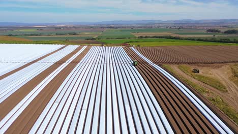 Aerial-Of-Tractors-Laying-Rows-Of-Plastic-Covering-On-Farm-Fields-Near-Santa-Maria-California-1