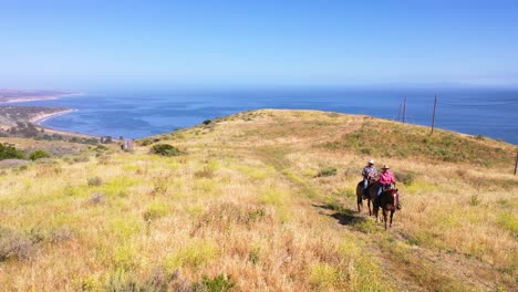 Aerial-Retired-Couple-Riding-Horses-At-Mountaintop-Overlook-Ocean-Or-Coastline-On-A-Ranch-Near-Santa-Barbara-California