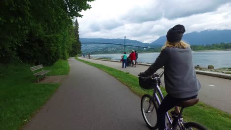 Eine-Fahrradkamera-Fängt-Die-Ansicht-Von-Hinten-Ein,-Während-Eine-Frau-Im-Stanley-Park-In-Vancouver-Mit-Dem-Fahrrad-Am-Ufer-Entlang-Fährt