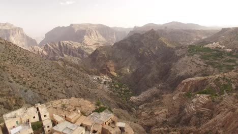 Una-Vista-Aérea-Muestra-Una-Ciudad-Escondida-En-Una-Región-Montañosa-De-Wadi-Shab-Omán