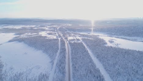 Eine-Luftaufnahme-Zeigt-Ein-Auto,-Das-In-Schweden-Eine-Von-Bäumen-Gesäumte,-Schneebedeckte-Autobahn-Entlangfährt
