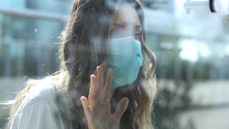 Eine-Gereinigte-Frau-Mit-Maske-Wird-Während-Der-Coronavirus-Pandemie-Durch-Ein-Glasfenster-Von-Einer-Geliebten-Person-Getrennt-Oder-Isoliert