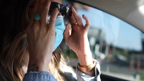 A-woman-puts-on-a-surgical-mask-before-driving-her-car-during-the-Covid19-coronavirus-pandemic-epidemic
