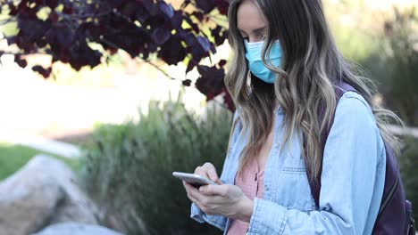 Eine-Frau-In-Einer-Maske,-Die-Während-Der-Covid19-Coronavirus-Pandemie-Epidemie-Mit-Ihrem-Telefon-Scrollt