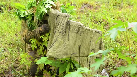 A-Camouflaged-Sniper-Student-And-His-Camouflaged-Rifle-Lie-In-Wait-In-A-Forest-At-Fort-Benning