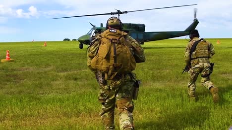 Soldaten-Rennen-Zu-Einem-Huey-Hubschrauber-Auf-Einer-Grasbewachsenen-Ebene-Mit-Uns-Service-Und-Truppen,-Die-Die-Mission-In-Zeitlupe-Bewachen