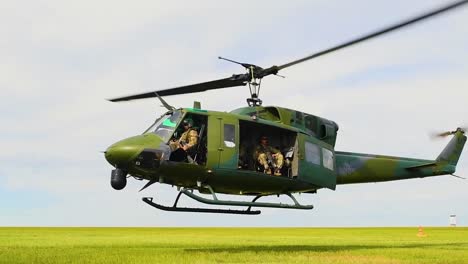 A-Huey-Helicopter-Hovers-Over-A-Grassy-Plain-With-Us-Servicement-And-Forces-Guarding-The-Mission-In-Slow-Motion