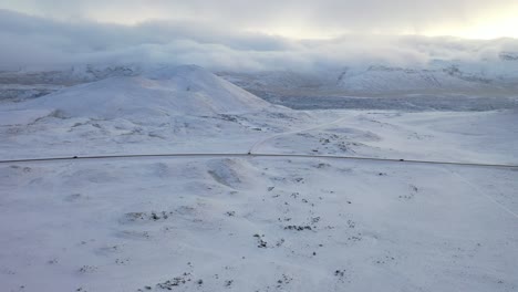 Aerial-of-cars-driving-along-a-snowcovered-highway-by-mountains-in-Iceland