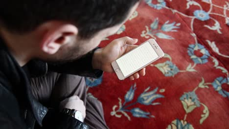Hombre-Musulmán-Leyendo-El-Corán-Con-Un-Teléfono-Móvil-En-Una-Mezquita