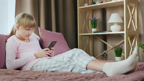 Blonde-girl-in-her-bed-uses-a-smartphone-1