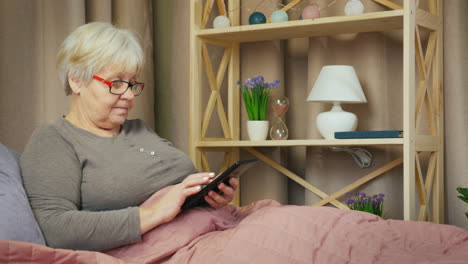 Older-woman-relaxes-in-her-room-and-uses-a-tablet