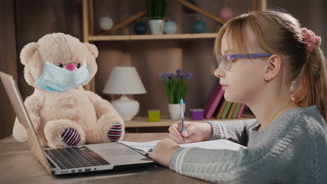 School-Pupil-Doing-Lessons-Online-With-Laptop-Next-To-A-Teddy-Bear-In-A-Protective-Mask