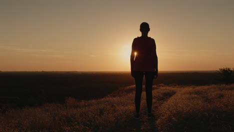 Slender-woman-stands-on-a-hill-in-the-rays-of-the-setting-sun