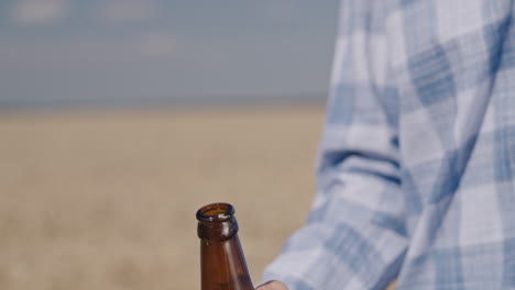 Man-opens-a-bottle-of-beer-with-wheat-field-in-the-background-1