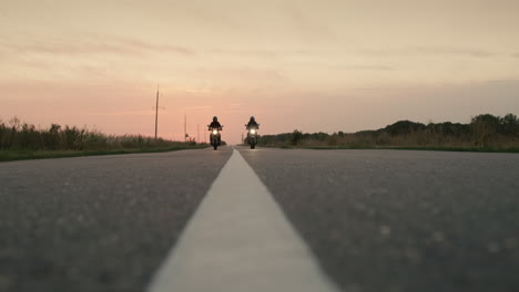 Two-motorcycles-drive-on-a-flat-highway-at-sunset