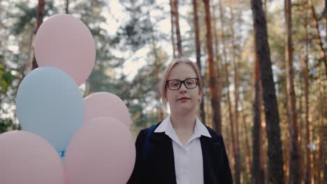 Portrait-of-a-schoolgirl-with-balloons-stands-in-a-park-with-high-pines