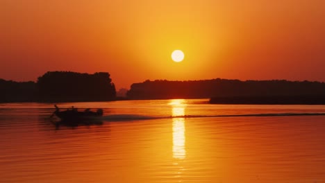 Silhouetten-Von-Menschen-In-Einem-Motorboot,-Das-Bei-Sonnenuntergang-Entlang-Des-Flusses-Segelt