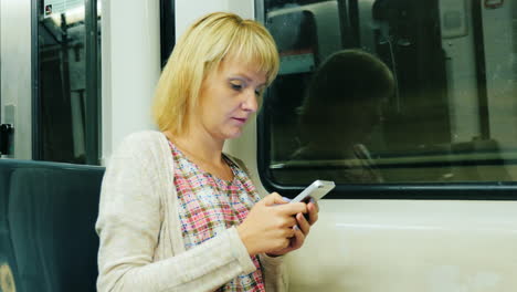 Eine-Frau-Fährt-In-Einem-U-Bahn-Wagen-Und-Benutzt-Ein-Smartphone