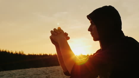 A-young-man-in-a-hood-prays-at-sunset