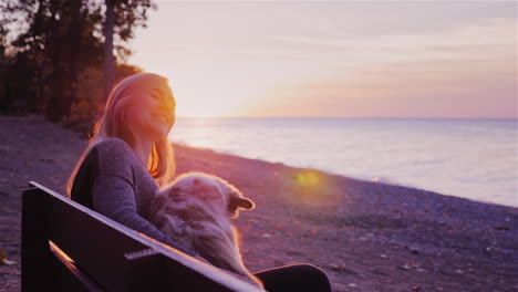 Eine-Frau-Ruht-Mit-Einem-Hund,-Der-Auf-Einer-Bank-Sitzt,-Vor-Dem-Hintergrund-Eines-Wunderschönen-Sonnenuntergangs-über-Dem-Ontariosee-2