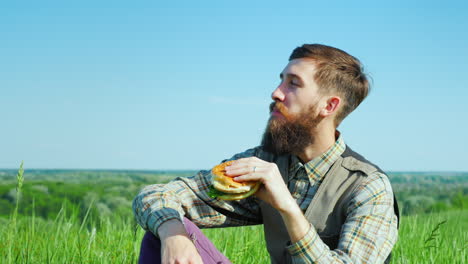 A-Young-Bearded-Man-Eating-A-Hamburger-Outdoors