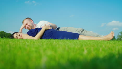 Young-Husband-With-His-Pregnant-Wife-Relaxing-In-The-Park-Together-Lie-On-The-Green-Grass