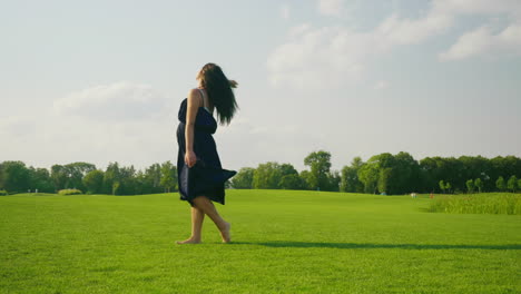 A-Stylish-Pregnant-Woman-In-A-Light-Dress-Carefree-Walks-Along-A-Green-Meadow-Past-The-Camera-1