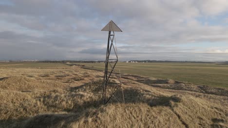 Coastal-tower-standing-on-sandy-dunes,-aerial-orbit-shot