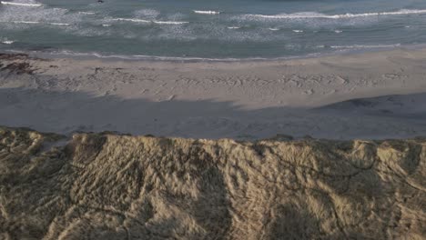 Ocean-waves-hitting-sandy-beach-and-majestic-dunes,-aerial-view