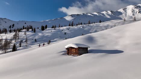 Two-alpine-ski-tourers-passing-an-old-hut-on-the-ascent