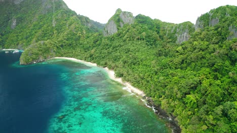Beautiful-white-paradise-beach-on-the-clear-blue-pacific-ocean-between-the-huge-green-jungle-and-large-gray-rocks-near-El-Nido-on-a-sunny-day