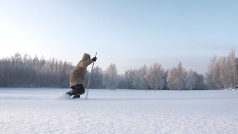 Sideview-of-man-with-stick-walking-in-deep-snow-in-arctic-winter-landscape