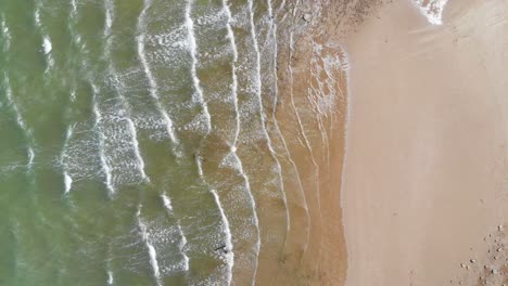 An-Einem-Warmen-Und-Sonnigen-Tag-Schiebt-Ein-Wunderschöner-Limonengrüner-Und-Aquablauer-Ozean-Kleine-Wellen-Auf-Einen-Strand-Aus-Sand,-Stein-Und-Mehreren-Kleinen-Felsen