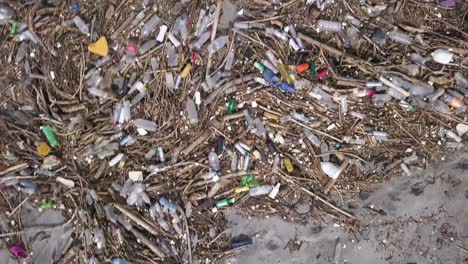 Trash-polluting-a-beach-with-many-plastic-bottles-and-other-waste---Aerial-directly-above-View