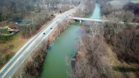 Aerial-view-of-cars-driving-along-a-road-nearby-a-forest-and-blue-water-river-in-Westfield-Hamilton-county-Indiana-USA