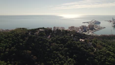 Aerial-view-Malaga-Port-with-sunlight-reflection-from-Mount-Gibralfaro-lush-vegetation,-Spain