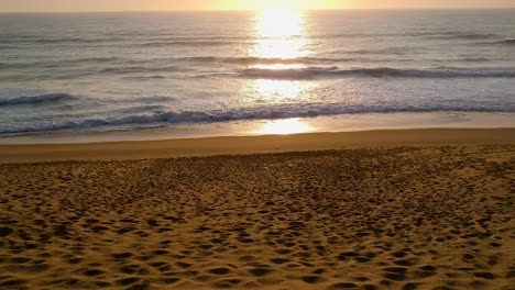 Sunset-beach-and-ocean-shot,-flying-slowly-towards-the-sun-setting-over-the-ocean