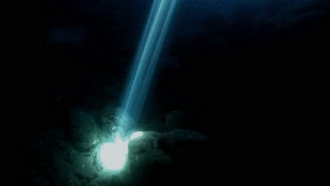 Exploring-the-dark-water-of-a-sea-cave-with-a-natural-beam-of-sun-light-illuminating-rocks-underwater-in-a-mysterious-atmosphere,-Vis-island,-Adriatic-Sea,-Croatia