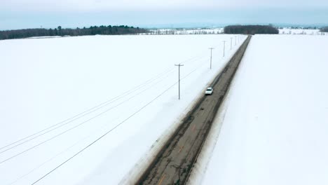 Aerial-view-of-a-car-driving-alone-on-a-winter-country-road