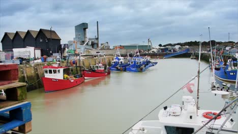 A-small-and-quintessentially-English-wharf-in-the-seaside-town-of-Whitstable-in-the-Shire-of-Kent,-with-pallets,-trawlers-and-other-small-boats