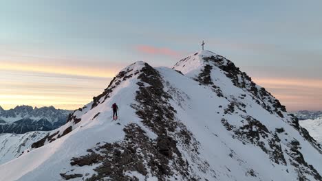 Snow-covered-mountain-shortly-before-sunrise-with-a-mountaineer-climbing-it-with-his-skis-in-the-Italian-Alps