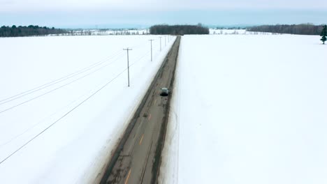 Drone-Siguiendo-La-Conducción-De-Un-Automóvil-En-Una-Carretera-Rural-En-Invierno