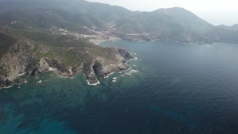 Aerial-shot-over-the-blue-waters-of-Argentiera-Cape-on-a-hazy-day