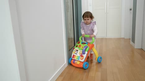 Süßes-Baby,-Das-Lernt,-Mit-Hilfe-Von-Sitz-zu-steh-walker-spielzeug-In-Einem-Hauskorridor-Zu-Laufen