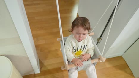 Upset-little-baby-girl-doesn't-want-to-swing-on-doorway-rope-swing-anymore---top-view