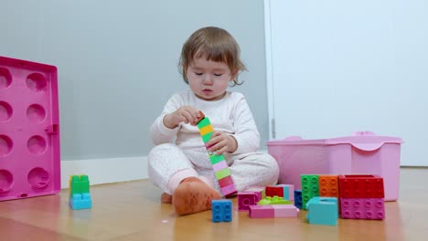 Adorable-two-years-old-toddler-girl-having-fun-making-tower-from-colorful-bricks