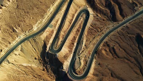 Four-vehicles-drive-downhill-on-the-black-asphalt-between-the-sharp-switchbacks-in-the-mountainous-landscape-of-sand-colored-Mitzpe-Ramon-in-Israel