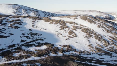 Aerial-drone-footage-flying-towards-a-rocky-mountain-landscape-covered-in-snow-near-Ben-Macdui-in-the-Cairngorms-National-Park,-Scotland-as-sunshine-reflects-off-of-a-snow-and-ice